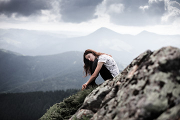 Naklejka na ściany i meble Young woman sitting on a mountain top. Woman hiking around mountains. Calm and inspiration on high peak of mountain