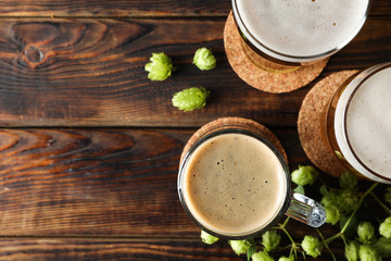 Mugs with beer and hop cones on wooden table, top view