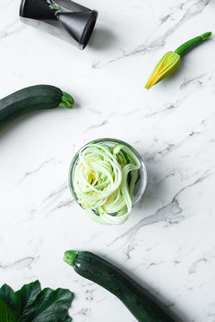 zucchini zoodles with fruit, flower and gadget on a marble backg