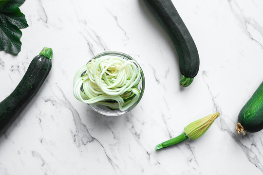zucchini zoodles with fruit, flower and gadget on a marble backg