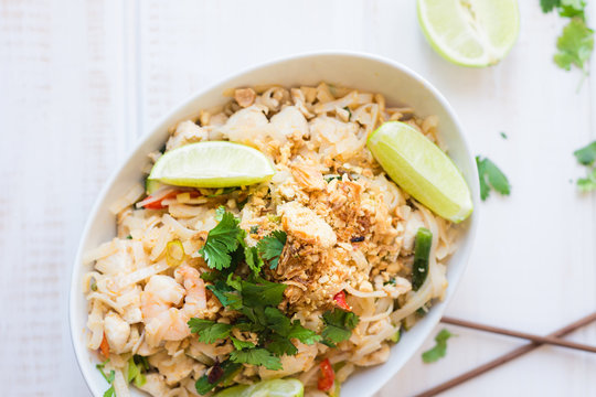pad thai in a white dish with garnish of coriander and lime