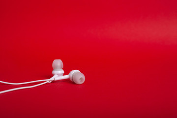Concept: white headphones (earphones) on a red background