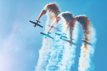 Three light-engine aircraft perform aerobatics - a dead loop. The bright sun illuminates the planes and the shadows fall on the smoke they leave in the sky. - obrazy, fototapety, plakaty