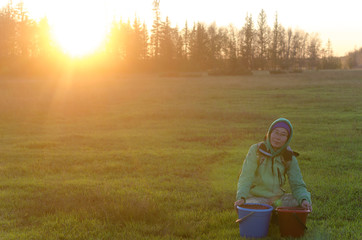 Yakut Asian girl in a hood and hat, Yves glasses sitting smiling in the shade on a green field...