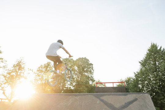 Young man riding BMX bike at skatepark at sunset
