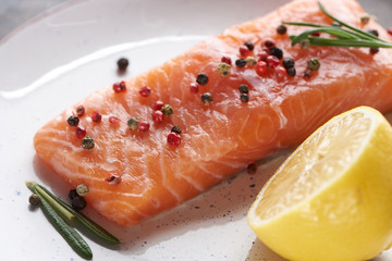close up view of raw fresh salmon with pepper, lemon and rosemary on plate