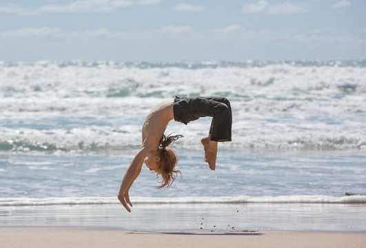 A redheaded boy back-flipping on a beach