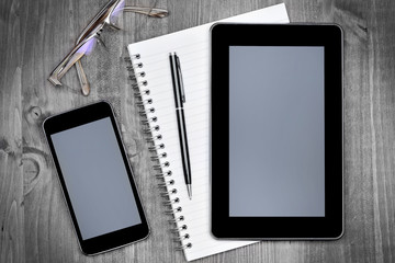 Empty digital tablet with notepad, phone and glasses on table