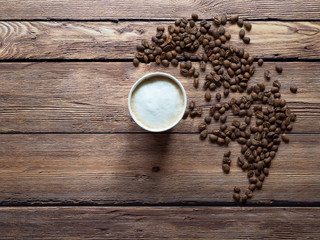Coffee in a paper cup is on the brown table.
