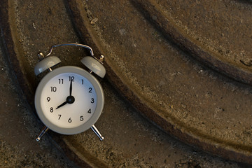 A clock with an alarm clock lies on a metal surface in the sun at dawn or sunset, morning or evening, and shows the time
