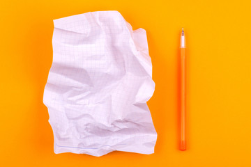 White crumpled sheet of paper with a notebook for texts, notes and drawings next to a yellow pen lies on an orange background