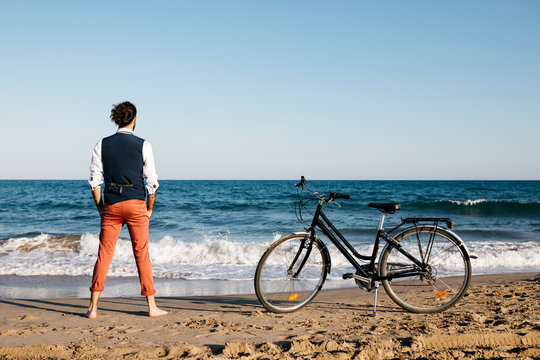Well dressed man with his bike standing on a beach
