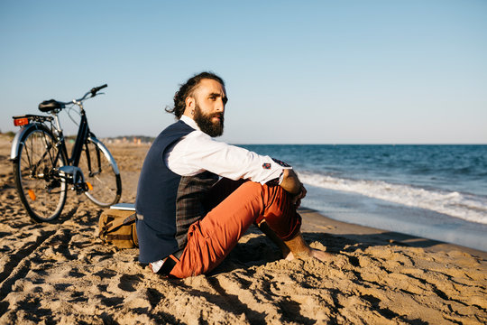 Well dressed man with his bike sitting on a beach