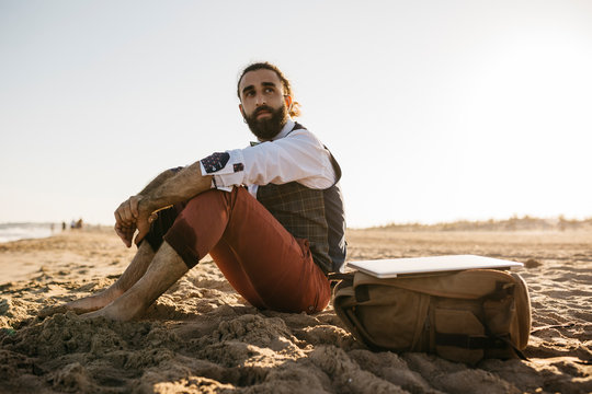 Well dressed man sitting on a beach looking around