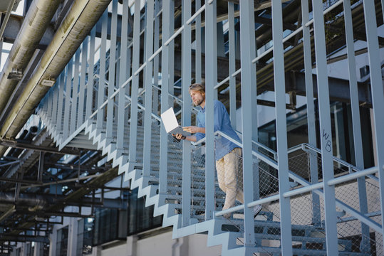 Young man standing on stairs using laptop