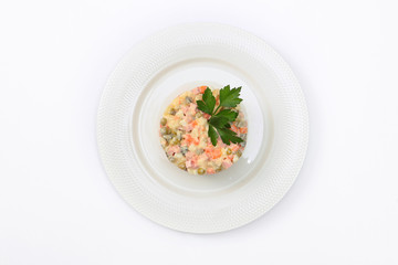 Russian traditional salad Olivier with parsley in a white plate on a white background top view. Concept of the New Year menu. Copy of space. Isolated object.