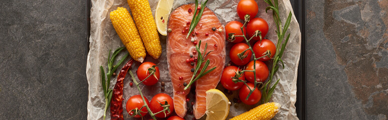 panoramic shot of raw salmon steak with tomatoes, corn, rosemary, lemon on bakery paper on oven tray