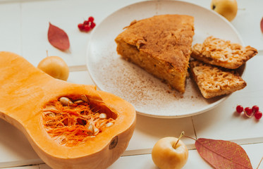  slice of pumpkin pie on a plate and pumpkin on a white wooden table. dry autumn leaves and yellow apples.
