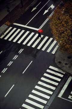 A woman with a red umbrella crossing the street