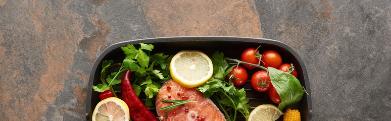 panoramic shot of raw salmon with vegetables, lemon and herbs in grill pan