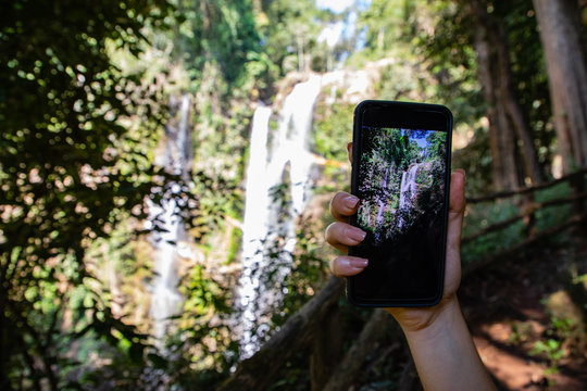 Woman hand holding a phone making a photograph of a waterfall