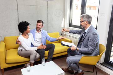 Young multiethnic couple at the office with real estate agent with key of new home in his hand