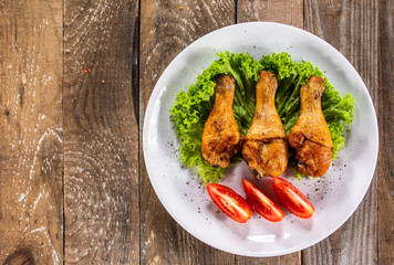 Fried chicken drumsticks with vegetables on wooden table