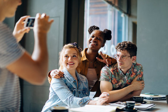 Students sitting in cafe, taking smartphone selfies - Powered by Adobe