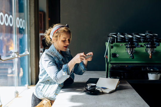 Young woman in coffee shop, using smartphone, taking pictures