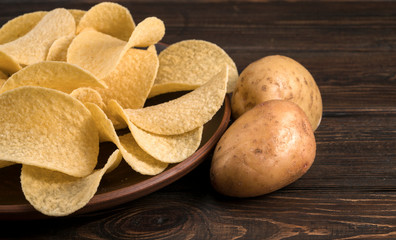 Potato chips in plate on wooden table isolated on brown background.
