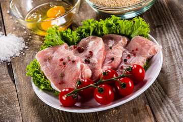 Raw pork chops and vegetables on white plate 
