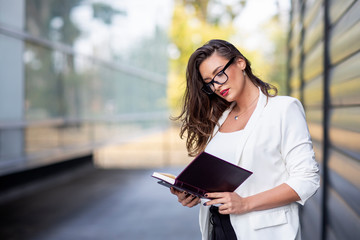 Obraz premium Business woman with glasses and paper notebook on hands standing in front of office building