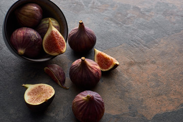 ripe whole and cut delicious figs scattered from bowl on stone background