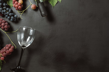 A bottle, wine glasses, fresh grapes and leaves on black background. Flat lay, top view, copy...