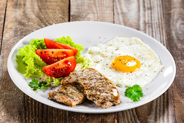 Grilled steaks with fried egg and vegetables on white plate