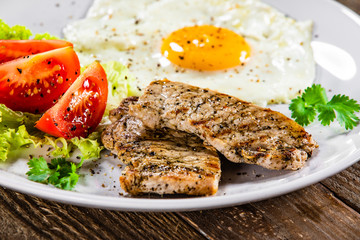 Grilled steaks with fried egg and vegetables on white plate