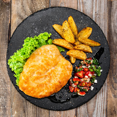 Fried pork chop, baked potatoes and vegetables on black stone plate