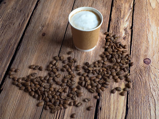 Coffee in a paper cup is on the brown table.