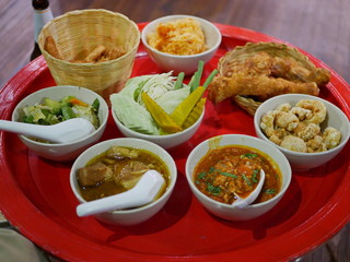 Northern Thai customary style dinner (khantoke) with variety of local menus being served family-style on large platters at low tables while guests relax on floor cushions