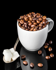 Full cup of coffee beans and spoon with sugar cubes on black.