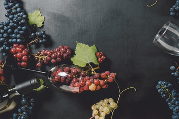 White wine bottle, wineglasses, fresh grapes and leaves on black wood background. Flat lay, top...