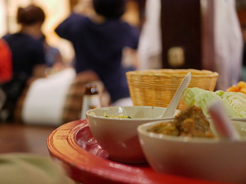 Selective focus of a Khantok dinner, Northern Thai style meal which people sit and eat on a floor, with blurry background of people at a party