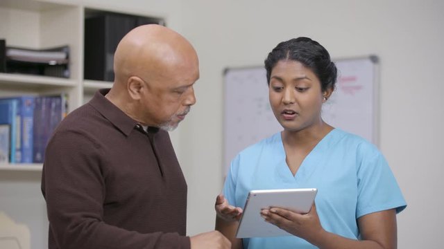 Nurse reviewing patient info on tablet at nursing station, camera move right