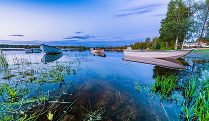 Motor and row boats anchored on the calm summer lake, sunset time, boats reflected in the water....