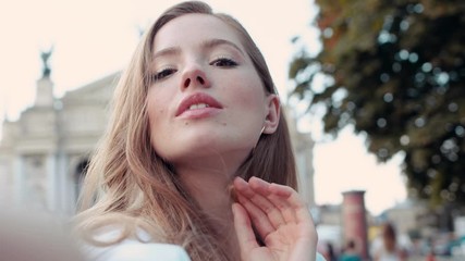 Lifestyle selfie portrait of young cheerful woman with curly golden hair posing and taking selfie on the street smiling and having fun