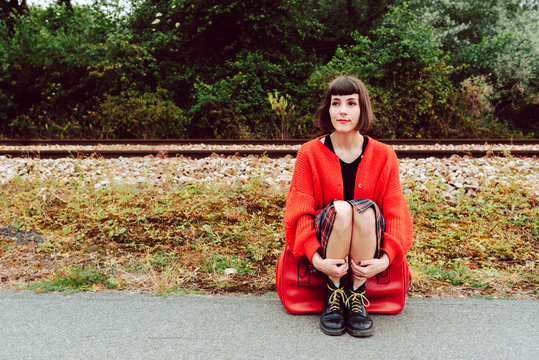 Woman sitting on red suitcase on road