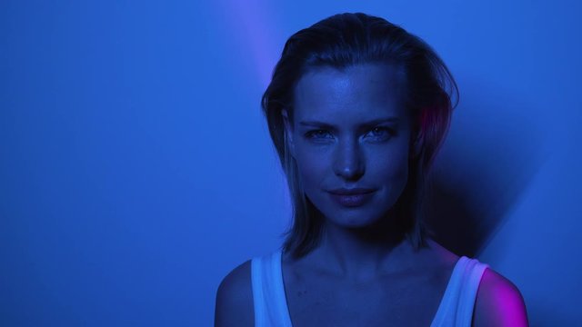 Beautiful Model in a Blue Dark Room Standing in Front of Wall with White Top