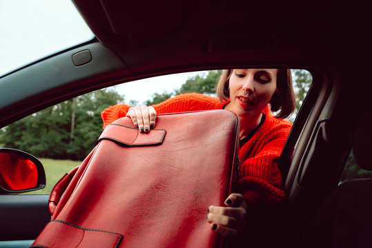 Diligent woman cleverly and skillfully stuffing suitcase into front seat of car through window