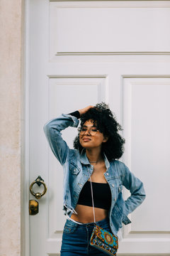 Trendy African American woman in black crop top and jeans standing by door and looking at camera