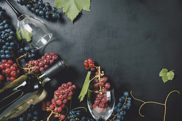 Bottle, two wine glasses, fresh grapes and leaves on black background. Flat lay, top view, copy space. Wine bar, winery, wine tasting concept